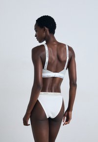 Fehér Calvin Klein melltartó és magasított derékú bugyi, logókkal díszítve, puha pamut anyagból készült, amely letisztult és minimalista dizájnt kínál.