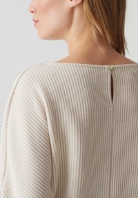 Top a righe beige e crema con collo rotondo, caratterizzato da un'apertura a chiave e un piccolo dettaglio con bottone sul retro. Tessuto dalla texture morbida.