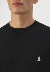 Sort bomulds t-shirt med rund hals og lille hvid flamme logo på venstre bryst. Glat tekstur med en klassisk pasform.