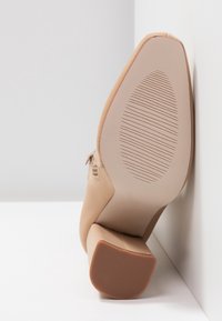 Chaussure à talons hauts beige avec une texture lisse, semblable à du cuir ; talon bloc solide ; bout légèrement pointu ; semelle en caoutchouc texturée pour une meilleure adhérence.