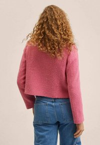 Chaqueta corta rosa con tejido texturizado, con cuello redondo y mangas largas, combinada con vaqueros azules de talle alto.