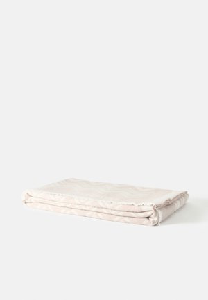 Couverture beige clair pliée avec des motifs subtils, posée à plat sur une surface blanche.