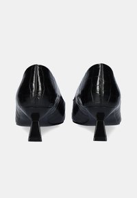 Tacones negros con grabado de cocodrilo que presentan una punta afilada y un tacón corto y robusto. La textura es brillante con sutiles acentos curvados a lo largo de los costados.