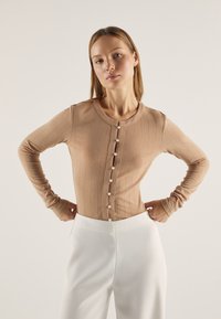 Beige ribbestrikket cardigan med lange ermer, rund hals og en rad med perleknapper foran. Figurtilpasset silhuett.