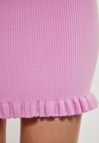 Gonna a maglia rosa a coste con dettagli di bordo arricciato. La texture sembra morbida e il tessuto ha una leggera lucentezza.