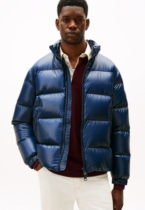 Navy blue, shiny puffer jacket with quilted sections, high collar, and zipper. Layered over a burgundy sweatshirt.