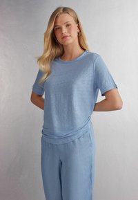 Světle modré triko s krátkým rukávem vyrobené z měkké látky, s volným střihem, v kombinaci se světle modrými kalhotami. Hladká, jednolitá textura.