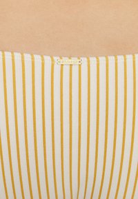 Artigo de tecido riscado em branco e amarelo, com finas linhas verticais. Inclui uma pequena etiqueta dourada com o logótipo "Billabong."