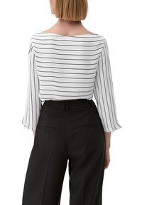 Camicia bianca con righe nere, scollatura ampia e maniche lunghe. Abbinata a pantaloni neri a vita alta con tasche posteriori.