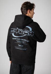 Black hoodie with a large blue graphic on the back, featuring text and logos. The fabric appears soft and has a relaxed fit.