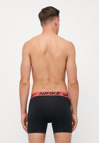 Sorte atletiske shorts med et rødt Nike-logo på taljen, med en glat tekstur og tætsiddende design.