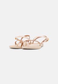 Tan vlakke sandalen met meerdere dunne banden, een gestructureerde binnenzool en een metallic accent op de verstelbare gesp. Eenvoudig en minimalistisch ontwerp.