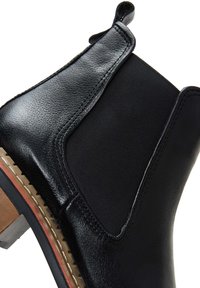 Botín negro de cuero con paneles laterales elásticos, detalles de costura y un tacón de madera con suela de goma. Textura suave y forma definida.