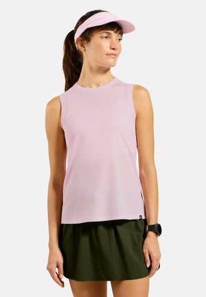 Woman wearing a light pink sleeveless top, dark green skirt, pink visor, and black smartwatch, standing against a plain light background.