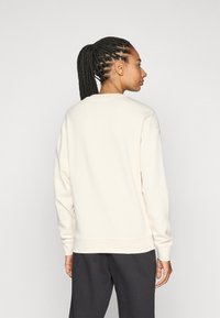 Cremfarbener Sweater mit rundem Ausschnitt und gerippten Bündchen. Locker sitzender Stil mit überschnittenen Schultern, aus weichem, strukturiertem Stoff gefertigt.