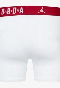Weiße Boxer-Shorts mit einem roten elastischen Bund, auf dem "AIR" in weißen Buchstaben gedruckt ist, sowie einem weißen Jumpman-Logo. Glatter Stoff mit angenehmer Textur.