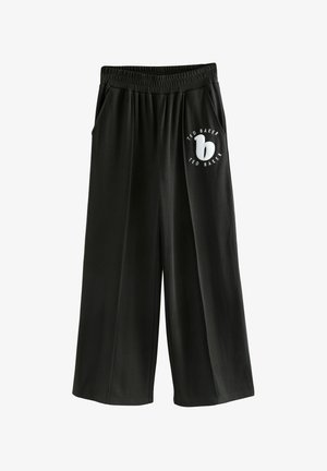 Pantaloni svasati neri in tessuto morbido con vita elastica, dotati di tasche laterali e di un logo circolare bianco con testo sul lato sinistro.