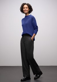 Blauer Strickpullover mit hohem Kragen, kombiniert mit dunkelgrauen, weit geschnittenen Hosen und schwarzen Schuhen, mit Taschen und lockerem Sitz.