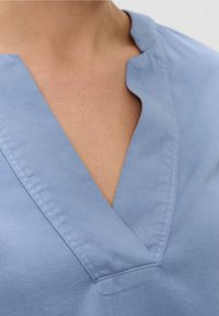 Camicia di cotone azzurro chiaro con design a V, caratterizzata da cuciture pulite e una texture liscia. La cucitura è visibile lungo il colletto.