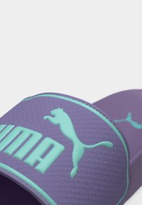 Μωβ σανδάλι με φάσα υφής που διαθέτει λογότυπο Puma σε τιρκουάζ και γράμματα.