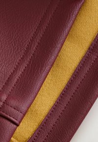 Burgundy bőrpanel textúrált felülettel, sima mustársárga filc szekcióval párosítva, látható varrással a széleken.