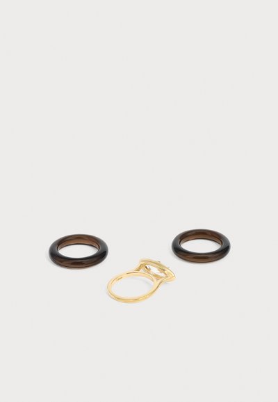 Deux bagues circulaires marron foncé et une bague en or avec une grande pierre précieuse claire sur fond blanc.