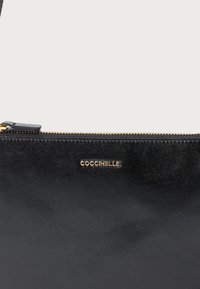 Mustast nahast kott tekstureeritud pinnaga. Omab kuldse tooniga tõmblukku ja esiküljel on embosseeritud logo. Kompaktne ja ristkülikukujuline.