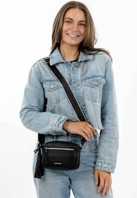 Black leather crossbody bag with textured finish, zippered pocket, and tassel detail. Adjustable strap, compact rectangular design.
