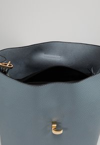 Emmertas in gestructureerd lichtblauw leer met een gouden metalen accent. De binnenkant heeft een zwarte voering en een ritszak.