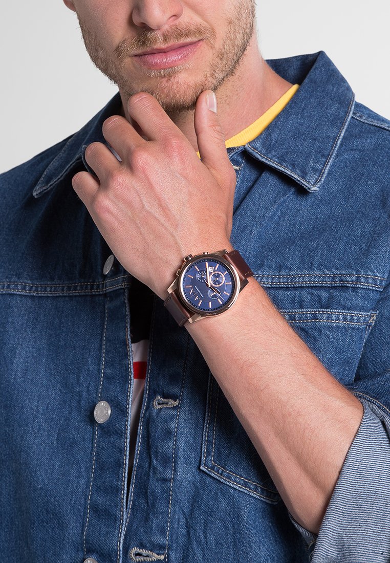 Brązowy skórzany zegarek z ciemnoniebieską tarczą, srebrnymi akcentami i funkcjami chronografu, noszony na nadgarstku na tle dżinsowej kurtki.