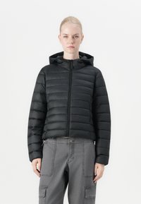 Svart polstret jakke med glidelås foran, hette og horisontal kviltedesign. Har elastiske mansjetter og cropped lengde. Kombinert med grå cargo-bukser.