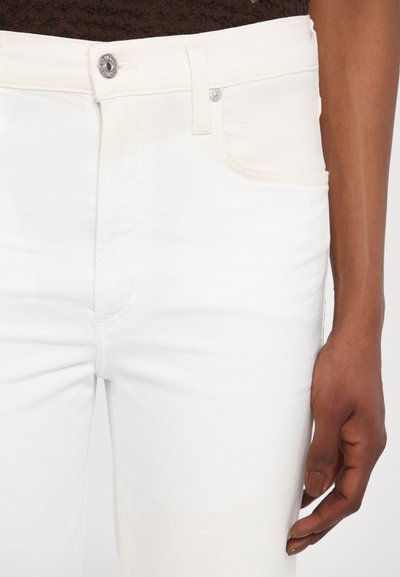 Jeans din denim alb cu un design ajustat, prezentând buzunare frontale, închidere cu un nasture argintiu și detalii fine de cusătură. Textură netedă.