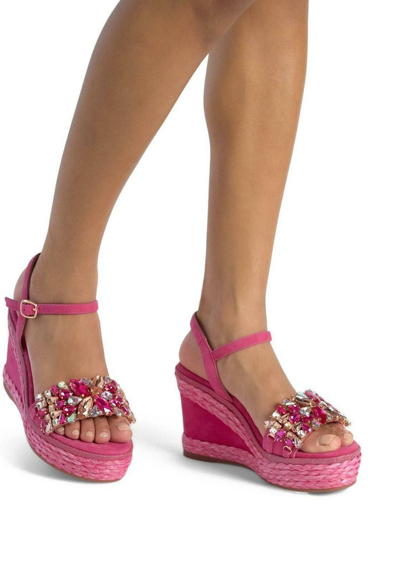 Sandales compensées rose vif avec un design à lanières, ornées de bijoux multicolores à l'avant, dotées d'une semelle en texture tissée.