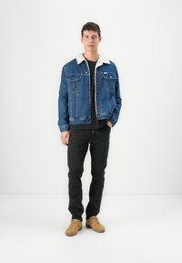 Denimjacket met een schapenwol kraag, blauwe kleur, voor sluiting met knopen en twee borstzakken. Draag het met zwarte jeans en tan schoenen.