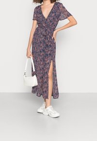 Abito a fiori con sfondo blu navy, motivi rosa e bianchi, maniche corte, scollatura a V e uno spacco laterale, abbinato a sneakers bianche.