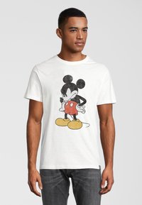 Camiseta de algodón blanca con un gráfico de Mickey Mouse en pantalones cortos rojos y zapatos amarillos, con detalles en negro. Diseño de cuello redondo.