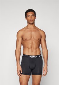 Black Nike boxers with a black waistband featuring white logo. The material appears smooth and fitted, with a moderate length design.