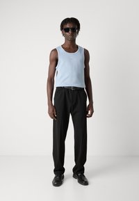 Débardeur bleu clair avec texture côtelée, associé à un pantalon noir, une ceinture noire et des chaussures noires, porté par une silhouette masculine, lunettes de soleil incluses.