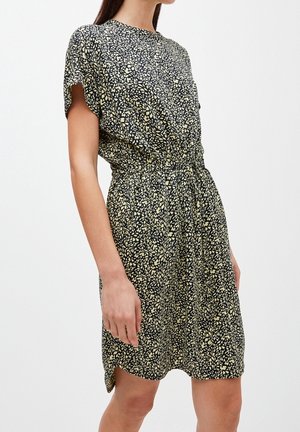 Frau trägt ein kurzärmeliges, knielanges schwarzes Kleid mit einem hellbeigen abstrakten Blumenmuster und einem elastischen Taillenbund.