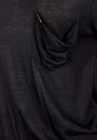 Maglietta nera a maniche corte realizzata in tessuto testurizzato con dettaglio della tasca drappeggiata, design minimalista e una delicata lucentezza.