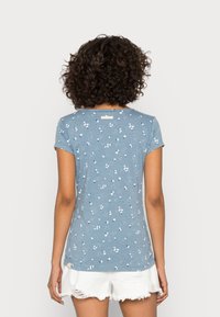 Niebieski t-shirt z krótkim rękawem w kwiatowy wzór i delikatne cętki. Miękka tkanina, okrągły dekolt i mała metka z tyłu.