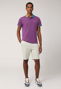 Lila polo tröja med mönstrad blå och gul krage, kombinerad med vita shorts och färgglada sneakers. Slät tyg, skräddarsydd passform.