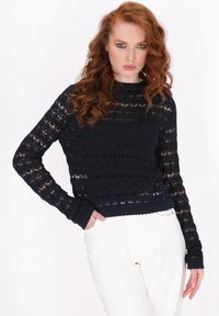 Granatowy sweter na szydełku z długimi rękawami, z otwartymi wzorami dzianiny i ściągaczami przy mankietach. Modelka pozuje na tle czystego białego tła.