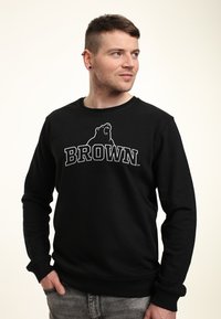 Zwarte sweatshirt met lange mouwen, ronde halslijn, voorzien van een berenlogo en de tekst "BROWN" in vetgedrukte witte letters over de borst.