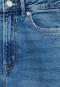 Vaqueros de mezclilla en azul claro con una textura desgastada, que cuentan con un bolsillo frontal, costuras de color cobre y un cierre de botón metálico.