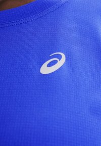 Μπλε αθλητική μπλούζα με υφή και μικρό λευκό λογότυπο Asics κοντά στη λαιμόκοψη.