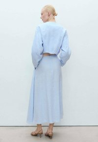 Helles blaues Leinen-Croptop mit voluminösen Ärmeln kombiniert mit einem fließenden Midikleid. Glatte Textur und minimaler Detail.