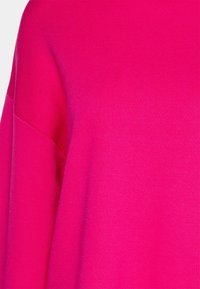 Suéter fucsia con una textura suave, que presenta un corte holgado y mangas oversized, exhibiendo un color sólido sin patrones ni acentos.
