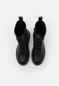 Botas de cuero negras con tobillo alto, punta redonda, cordones en la parte frontal y cremallera lateral. Presentan una superficie texturizada y suela de goma plana.