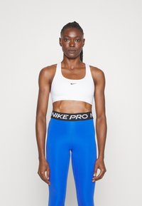 White sports bra with black Nike logo, paired with high-waisted blue leggings featuring black 'NIKE PRO' waistband. Smooth, fitted fabric.